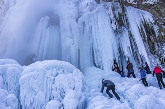 Spectators climb on the Urach waterfall full of bizarre ice formations, frozen at low winter