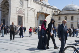 People wearing traditional clothes walking on a sunny square in front of historic buildings with