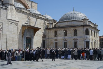 People gather in front of a large stone building with domes on a sunny day, prayer in front of the