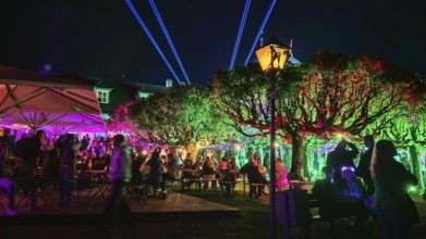 Colourfully lit garden at night, full of people, with atmospheric lighting, Kronach glows,