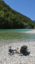 A bicycle is lying on a pebble beach by a river with clear water and wooded banks, Soca Valley,