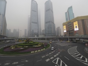 City scene with roundabout and skyscrapers in fog under grey sky, Pudong, Shanghai, China