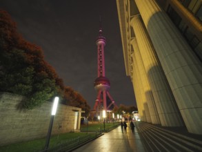 Illuminated television tower, Oriental Pearl Tower, in a nighttime street scene with people passing