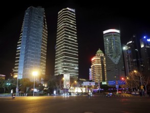 Illuminated skyscrapers in a modern city at night, with empty, well-lit street in the foreground,