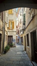 Narrow alley with historic buildings and colorful shutters in a sunny old town, Piran, Slovenia