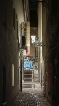 Narrow, illuminated alley at night with stairs lined with graffiti and old architecture, Ljubljana,