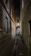 Dark, narrow alley at night with cobblestones and dim lantern light, urban atmosphere, Ljubljana,
