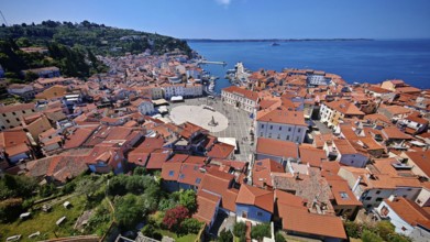 Panoramic view of a coastal town with a main square and red roofs on a clear blue day, Piran,