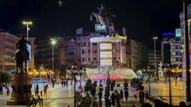 Illuminated square at night with equestrian statue and bubbling fountain in an urban setting,