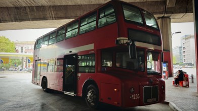 Classic red double-decker bus at a bus stop in an urban environment under a bridge, Skopje, North