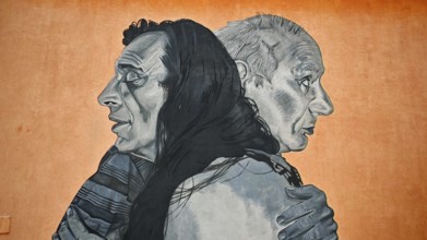 Large mural with two people hugging against an orange background, Pristina, Kosovo