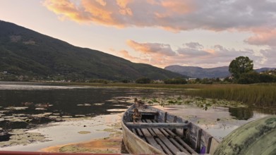 A boat on a lake with pink clouds and mountains evoking a peaceful evening, Lake Plav, Montenegro