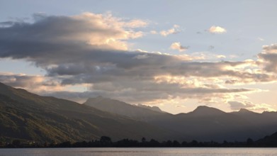 View of a mountain range with clouds glowing over a calm lake in the evening light, Plav Lake,