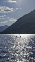 A lonely boat on a sparkling lake with mountains in the background and sunny atmosphere, Lake Plav,