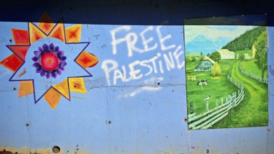 Wall art with graffiti free Palestine and a picture of a green landscape with houses and mountains,
