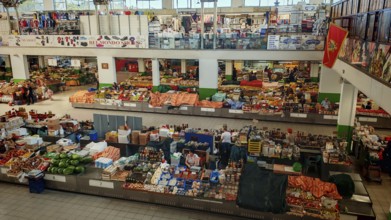 Large market hall with numerous stands and products. People buy fresh food. Lively atmosphere,