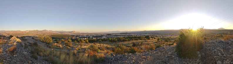 A city surrounded by nature with trees in the foreground and mountains in the background,