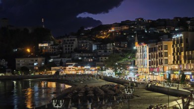A nighttime beach view with illuminated buildings and dark skies in a lively coastal town, Ulcinj