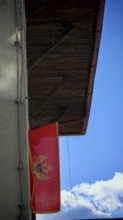 A Montenegrin flag flies on a wooden roof under a clear blue sky, Montenegro