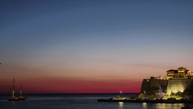 A sailboat sails under a colorful sky at sunset on calm sea, Ulcinj, Montenegro