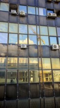 Reflections of clouds and cranes in a glass façade of a high-rise building, Pristina, Kosovo