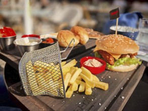 Burger with fries served on a wooden tray, with cheddar cheese, lettuce and tomatoes, in a sunny