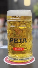 Clear beer glass with foam crown on a table in a lively environment, Peja, Kosovo