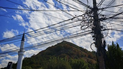 Several power lines in front of a minaret and a wooded hill, Prizren, Kosovo