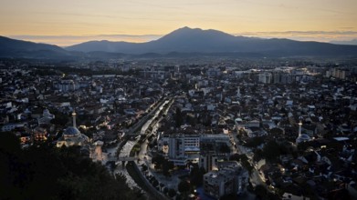 Night view of city with glowing lights, river and mountain skyline in the background, Prizren,