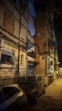 Night view of a city street with parked cars and worn buildings, Tirana, Albania