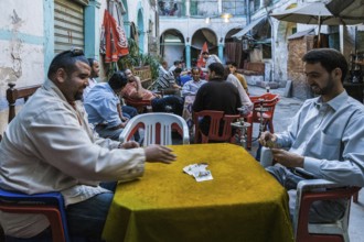 Tripoli, Libya, North Africa. Man playing cards and others smoking shisha in a traditional 'funduq'