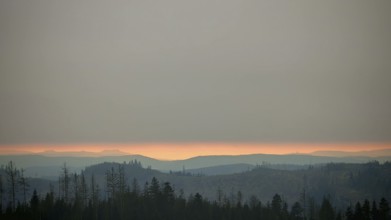 Forest and mountains at dusk below a cloudy horizon, with Staffelberg on a glowing horizon,