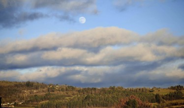 A peaceful landscape with forest and moon in a blue sky, surrounded by clouds, Franconian Forest