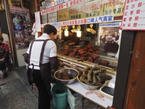 A saleswoman stands at a busy market stall with a variety of exotic foods, Zhujiajiao Ancient Town,