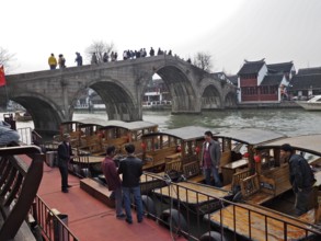 People on a stone bridge admire the wooden boats on the river in a historic city setting,