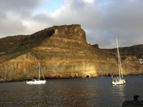 Rocks on calm sea with boats and golden evening sun, Puerto de Mogan, Gran Canaria, Canary Islands,