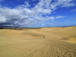 Large dune landscape with footprints and a hiker under a blue sky with white clouds, dunes of