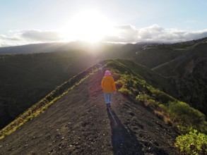 Female hiker walks along a sunlit hill with extensive shadows, Caldera de Bandama volcanic crater,