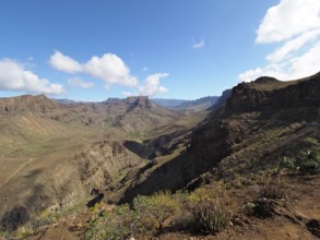 Arid mountain landscape with rocks and wide valley under a blue sky with clouds, Barranco de