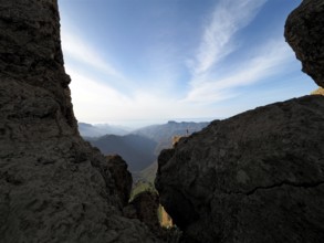 View through rocks of a vast mountain landscape under clear sky, Roque Nublo, Gran Canaria, Canary