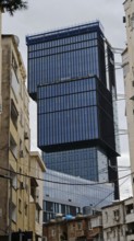 Modern high-rise building with glass façade between older buildings in an urban environment under