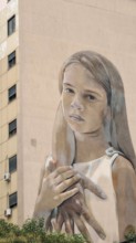 Large mural of a thoughtful girl on the façade of a building with natural facial expression,