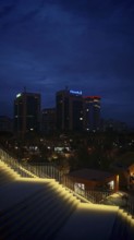 Nighttime city view with illuminated buildings and illuminated staircases in the foreground,