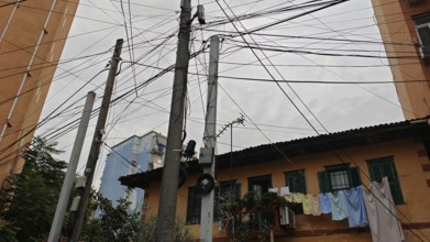 Power poles with a tangle of wires, next to buildings and clotheslines, create an urban image,