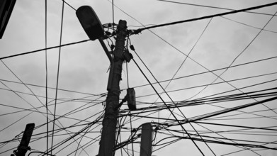 Black and white shot of numerous wires twisting around a power pole against a cloudy sky, Tirana,