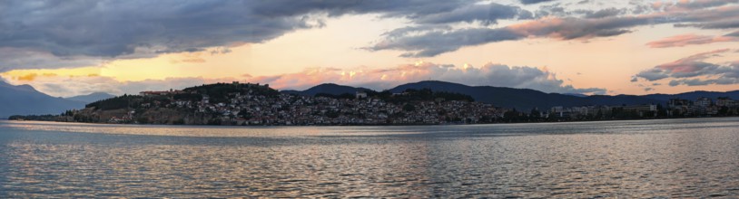 Evening panorama of a lake with mountains and a city in the background under dramatic sky, Lake