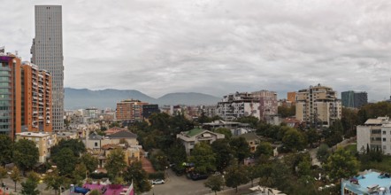 Urban panorama with modern high-rise buildings and mountains in the background on a cloudy day.