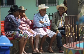 Guatemalan men wearing Coxboy hats sitting laughing on a bench in Santiago de Atitlán, Sololá