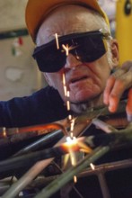Old worker, welder, metal construction, working into old age, pensioner, car, safety glasses,