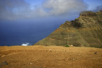 Rocky cliff with a cross in the ground, sea and clouds in the background, Mirador de Ermita de Las